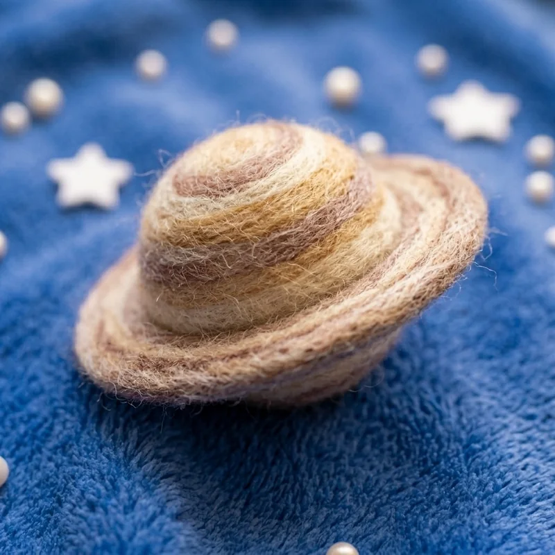 A needle-felted wool Saturn resting on the fleece blanket